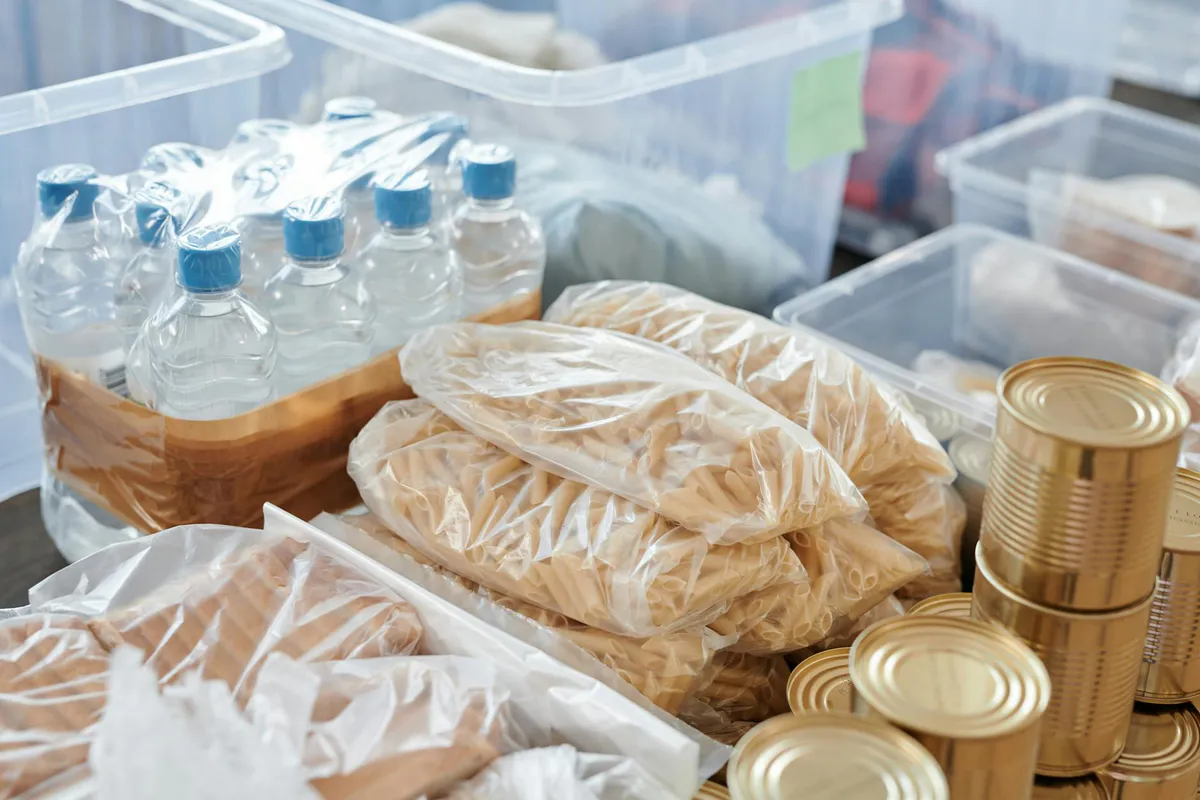 Storage shelf holding canned goods, sealed dry food packages, and bottled water arranged together