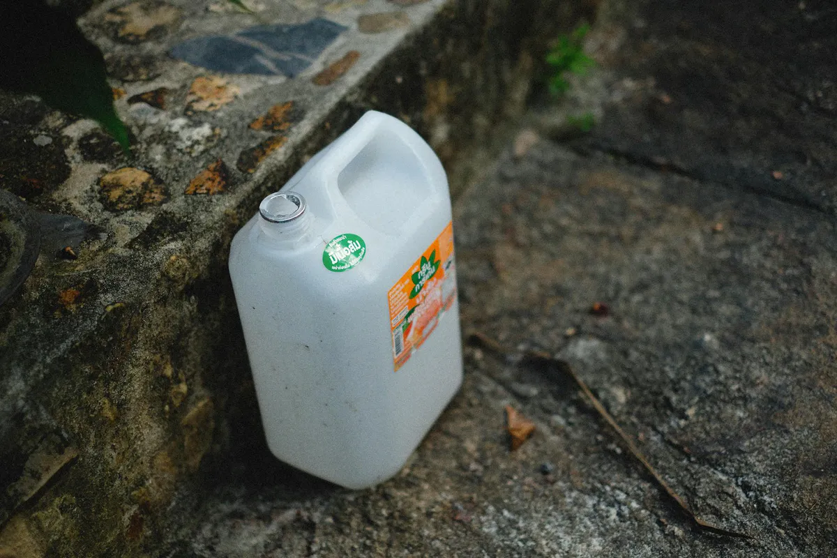 A large white food-grade plastic water container sitting on a stone surface outdoors