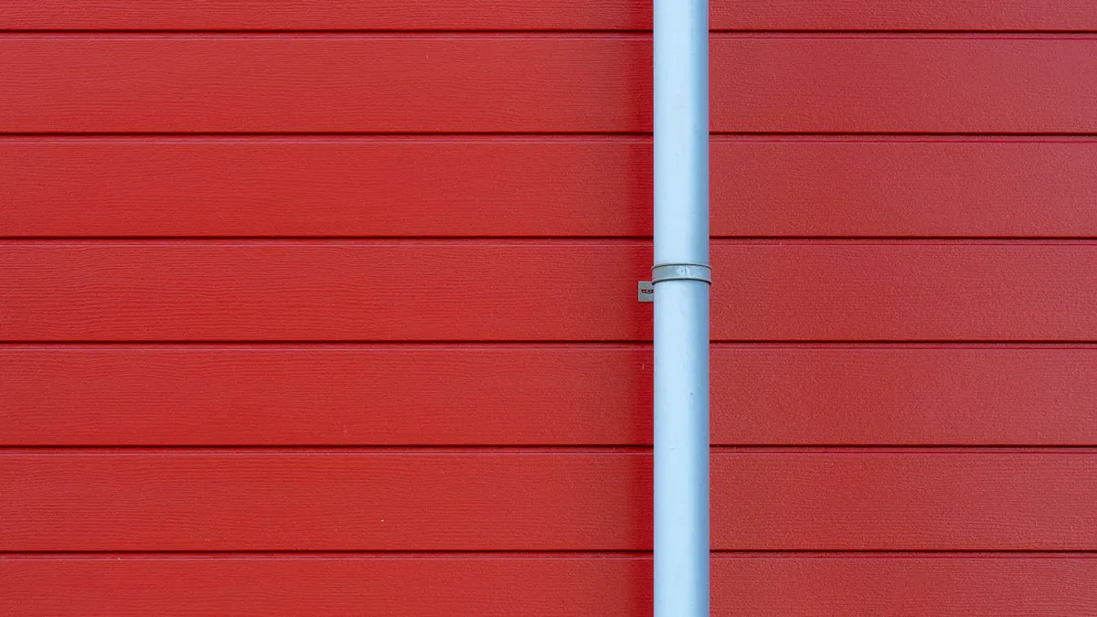 White gutter and downspout running down an exterior wall where a rain barrel diverter would attach