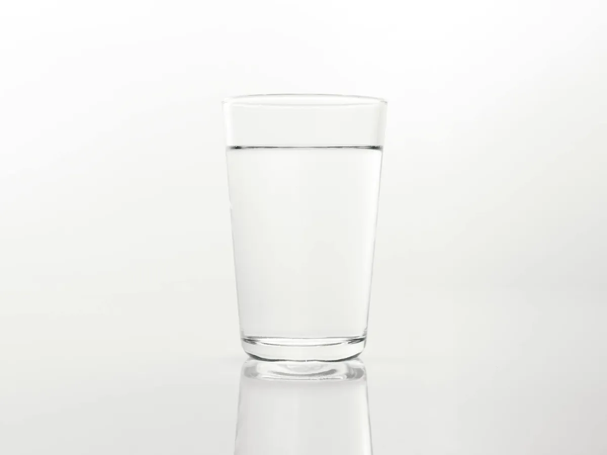 A single clear glass of water sitting on a plain reflective surface